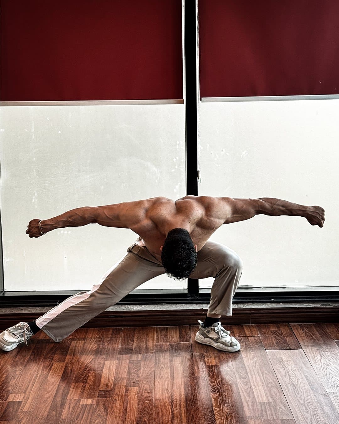 Rear view, arms spread wide in a low lunge, showing back development