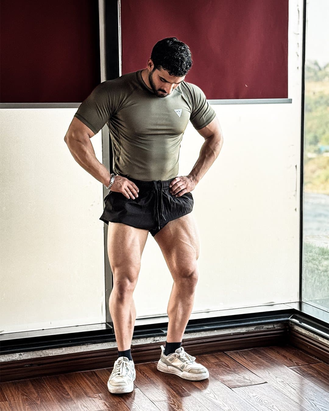 Asfand in an olive compression tee, hands on hips, looking down