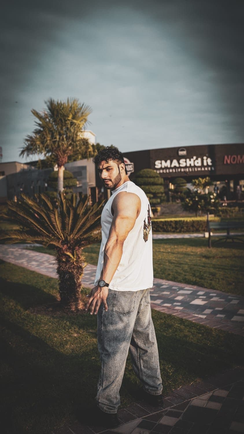 Asfand Khan outdoors at golden hour in a white sleeveless tee, looking back