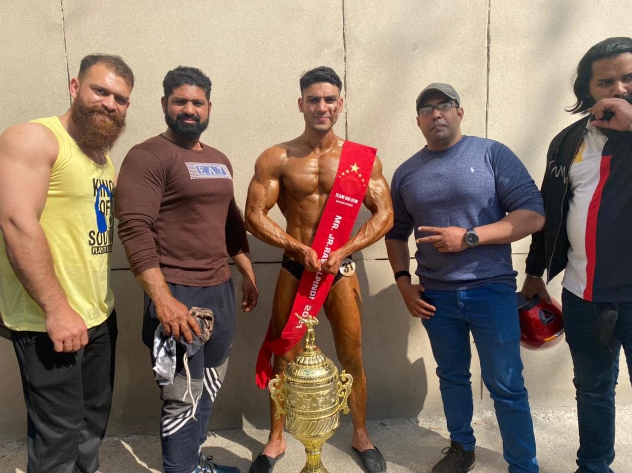 Asfand Khan with his team after winning Mr. Jr. Rawalpindi, trophy in front